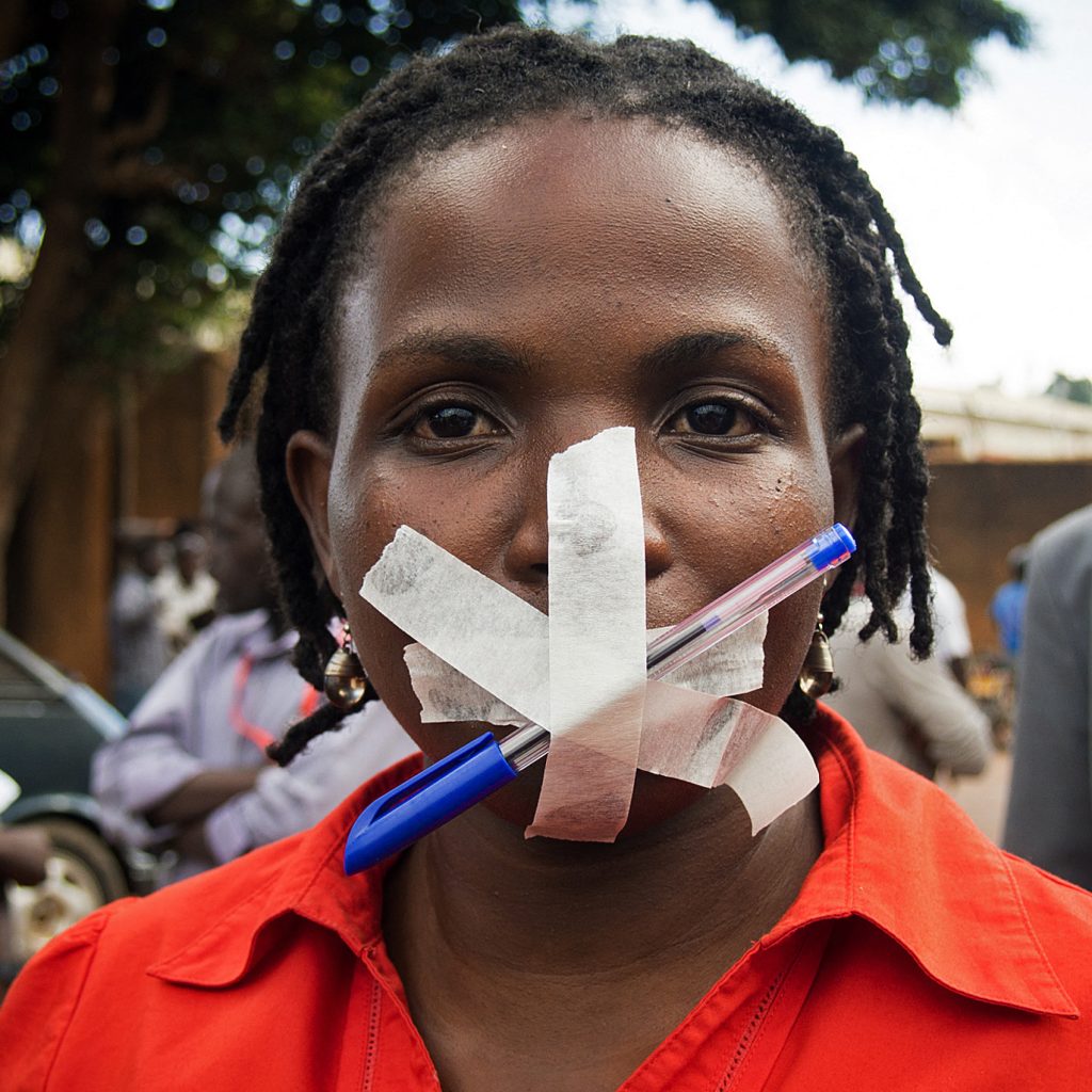 Femme avec la bouche couverte de ruban adhésif percé d'un stylo au milieu.