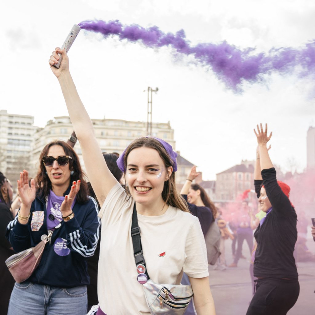 Femme souriante tenant un fumigène à la main lors d'une manifestation.